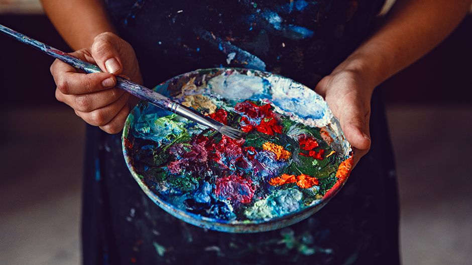 Two hands holding a palette of colorful paint and a brush