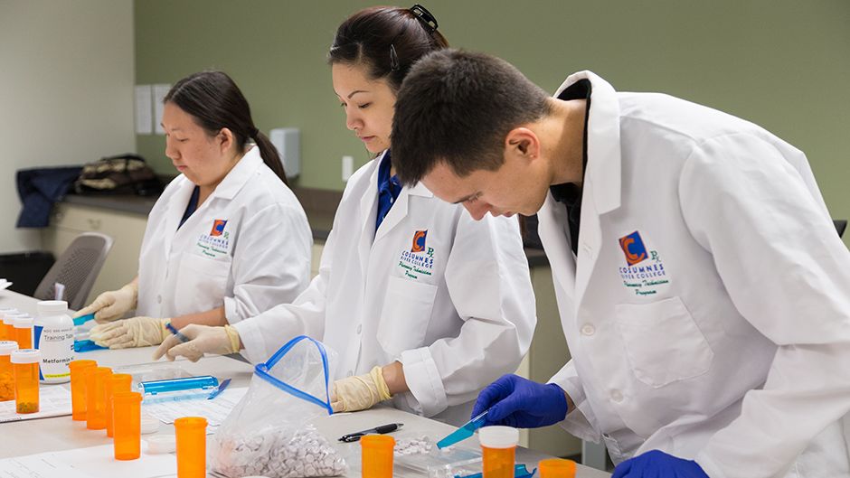 Three students in lab coats sorting medication