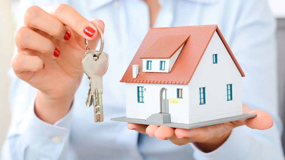 A person holding keys and a miniature house
