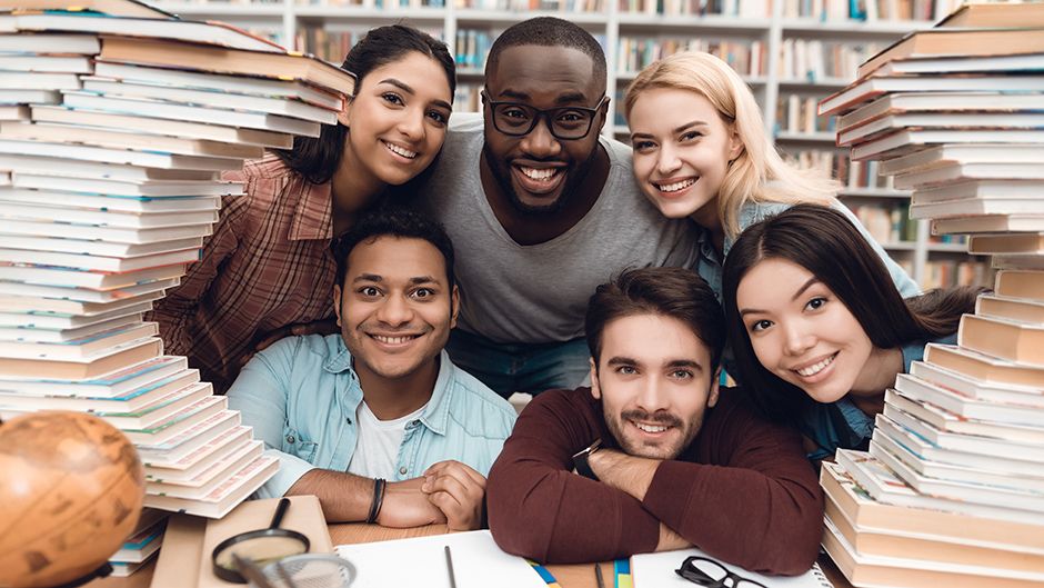 A group of diverse students peeking around a stack of books